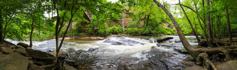  a stunning panoramic shot of the rushing river water of Big Creek river with lush green trees and large rocks on the banks and in the middle of the river at Vickery Creek in Roswell Georgia © Marcus Jones
