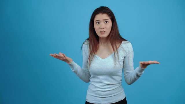 The irritated girl waved her hands in parts and looked questioningly in parts, what is this. Asian with dark hair, dressed in a blue blouse, isolated on a dark blue background in the studio. The