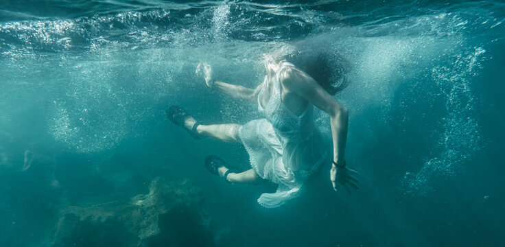 Image of a young woman with a white dress diving into the sea, underwater image, summer lifestyle of a young Caucasian brunette