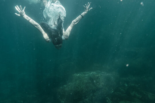 Image of a young woman diving with a white dress diving, underwater image, summer lifestyle of a young Caucasian brunette