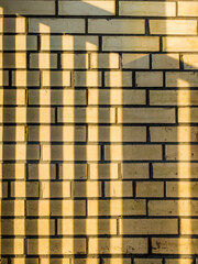 Horizontal, striped shadow on a yellow brick wall. Smooth, horizontal sunbeams. Unusual texture