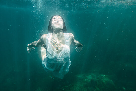 Image of a young woman diving with a white dress diving, underwater image, summer lifestyle of a young Caucasian brunette
