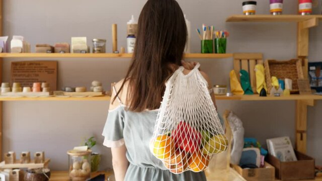 Woman in a store with a string bag of fresh food, no packaging with pasta, nuts and grains, natural soap in a store without plastic waste. Low-waste lifestyle. Sustainable ecological lifestyle