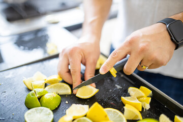 Male hands slicing lemons and limes on a black tray