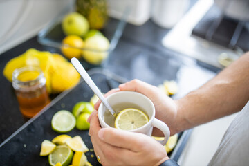 Male hands holding a cup of lemon tea above lime slices