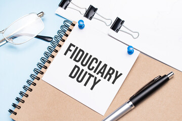 Notepad with fiduciary duty text on the office table with glasses, notepad and paper with clips. - obrazy, fototapety, plakaty