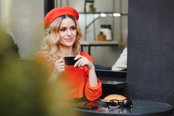 Young stylish woman in red beret having a french breakfast with coffee and croissant sitting oudoors at the cafe terrace - obrazy, fototapety, plakaty