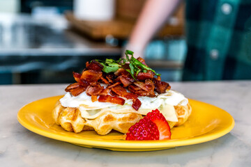 Belgium waffle with whip creme strawberries and bacon served on a yellow plate