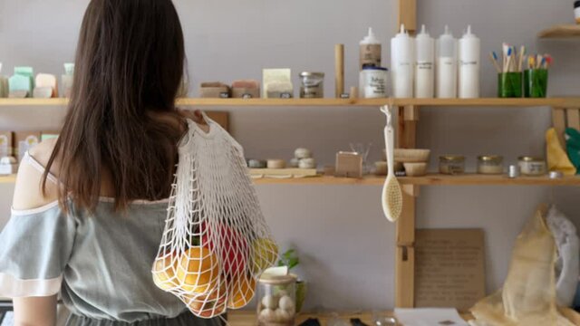 Woman in a store with a string bag of fresh food, no packaging with pasta, nuts and grains, natural soap in a store without plastic waste. Low-waste lifestyle. Sustainable ecological lifestyle