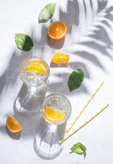 A glass of mineral water and a slice of orange on a gray table with fresh juicy fruit oranges with hard shadows. Summer time. Top view