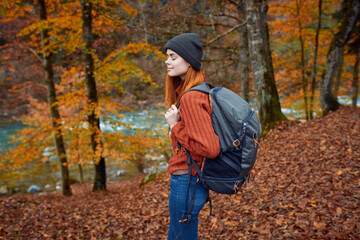 woman with backpack walking in the autumn park near the river in nature side view