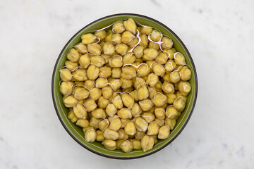 Chickpeas soaked in water, in bowl, on marble table. Concept of healthy eating, veganism, vegetarianism, meat and egg replacement. Prepare chickpeas before making hummus and other legume dishes