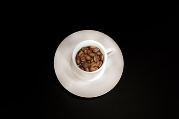 Coffee beans in a white coffee cup on a black background, top view
