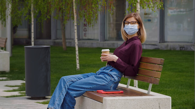 Business Caucasian Woman Wearing Medical Mask Takes A Break. Outdoor Relaxing Break From Work Enjoys Sunny Spring Summer Day Coffee Break. Lady Looks Thoughtful And Enjoying Coffee. 