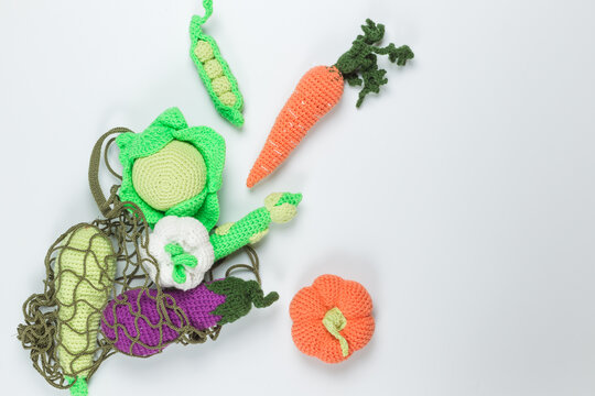 Children's food. A game set of knitted vegetables in an eco-friendly string bag. Flatlay on a white background