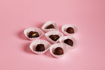 Composition of chocolate truffles and pralines in paper wrappers on pink background with copy space