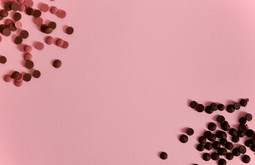 Flat lay composition with scattered pink and dark chocolate pills in corners of pink background with copy space