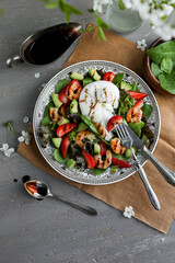 Shrimp, spinach, strawberry and burrata salad in a large vintage plate on a gray table. Healthy food with vegetables, cheese and seafood. Flat lay.