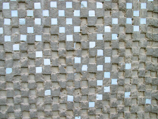 An old gray wall of a house with small squares of blue smalt arranged in a checkerboard pattern....