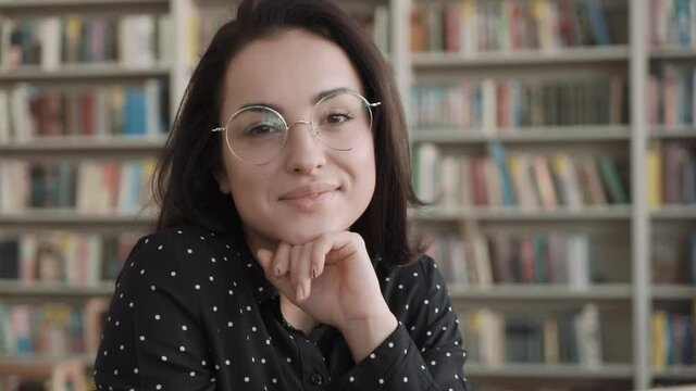 Portrait of beautiful young woman wearing glasses, bookshelf on background