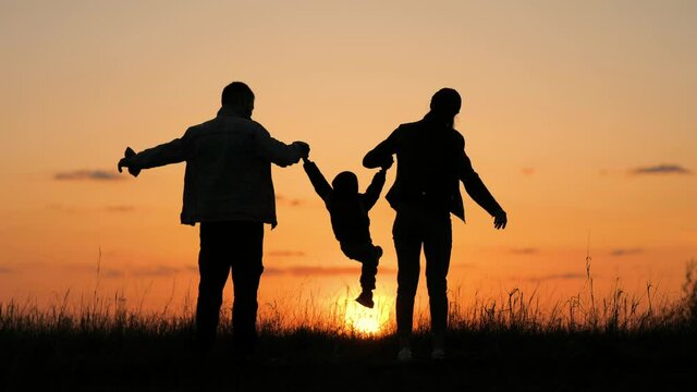 Happy family, parents and little son silhouettes playing on park. Silhouette family running at sunset. Teamwork child and parents run fun in the park. Friendly family and teamwork kid dream concept.
