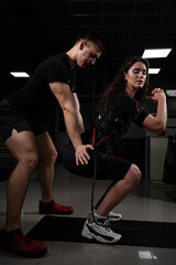 Man trainer trains a girl in an EMS suit in the gym. Electrical stimulation of the misc during active training