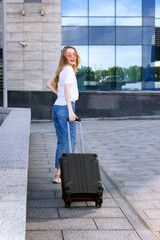 Attractive girl with glasses with a suitcase goes to the airport in the summer. travel and vacation