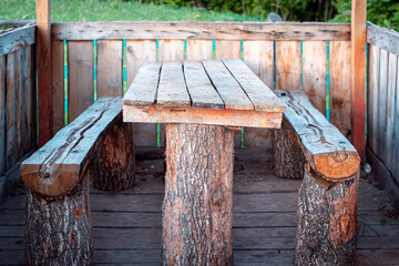 A table and a bench made of wood in a gazebo in the forest.