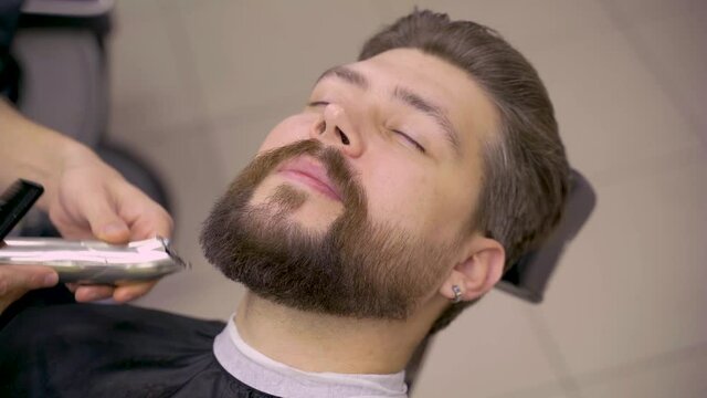 Barber is shaving beard and mustache for handsome customer. Trimming beard in barbershop