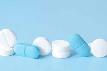 White and blue tablets and pills on a light blue background. Medical concept. Selective focus