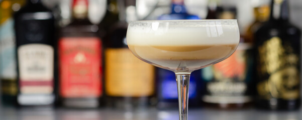 Alcoholic coffee cocktail with a nutty note and fluffy milk foam on the background of the bottles at the bar