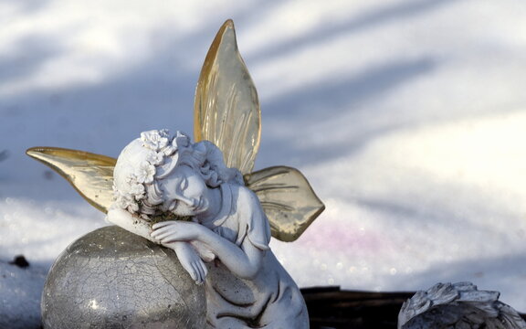Schlafender, weißer Engel auf einem Grab im Schnee