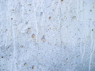 An old bluish-gray uneven wall of a house with cracks and scratches with holes. Small shells are worn.
