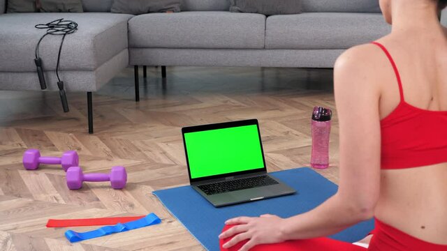 Green screen mock up chroma key monitor laptop: Fit fitness woman in sportswear sits on yoga mat doing warm-up before workout exercise training, online sport lesson course video call webcam computer