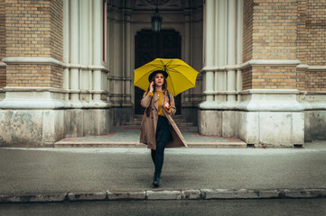 Woman using smartphone and holding a yellow umbrella on a rainy day