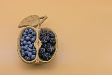 Wooden bowl filed with blueberries and blackberries, yellow background