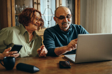 Senior couple using a smartphone and a laptop while relaxing at home