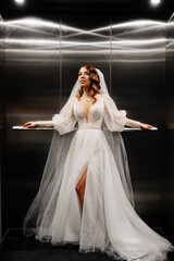 bride in a white elegant dress, with a long veil stands in a dark lift.