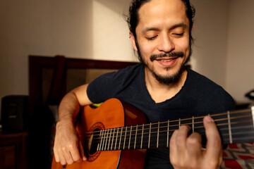 Young latin man playing guitar at home in the bedroom
