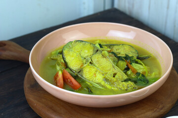 Pindang Ikan Patin or Catfish vegetables Soup , Indonesian food popular from Palembang. Served on ceramic bowl garnished wit tomato slices. Copy space for text. Dark wooden background. 