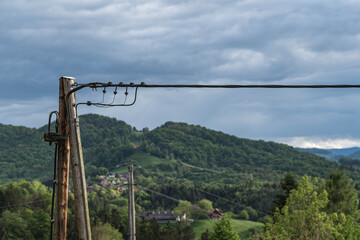 Holzmast und Stromleitung vor hügeligem Wald