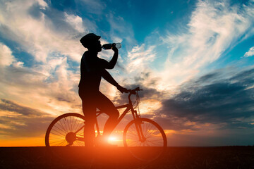 Silhouette of a cyclist drink water have a rest against the beautiful sunset.