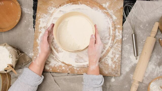 female hands sift white wheat flour through a wooden round sieve, top view on a table with ingredients