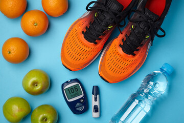 Orange sneakers, apples, oranges and a blood glucose meter on a blue background