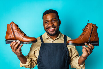 latin hispanic man in black apron showing brown leather shoes in blue studio background