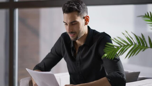 Angry stressed anxious man throwing away documents sitting on armchair at window in home office. Portrait of handsome young worried Middle Eastern businessman having problems thinking
