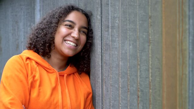 Beautiful mixed race African American girl teenager young woman looking sad then laughing and happy wearing an orange hoodie in an urban city environment
