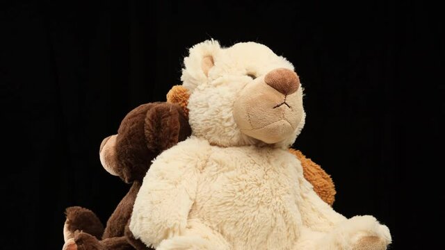three plush toy bears of different sizes rotate on a black background. Kids toy