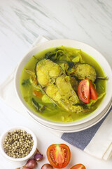 Pindang Ikan Patin or Catfish vegetables Soup , Indonesian food popular from Palembang. Served on ceramic bowl garnished with tomato slices. White marble background.