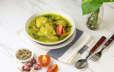Pindang Ikan Patin or Catfish vegetables Soup , Indonesian food popular from Palembang. Served on ceramic bowl garnished with tomato slices. White marble background.